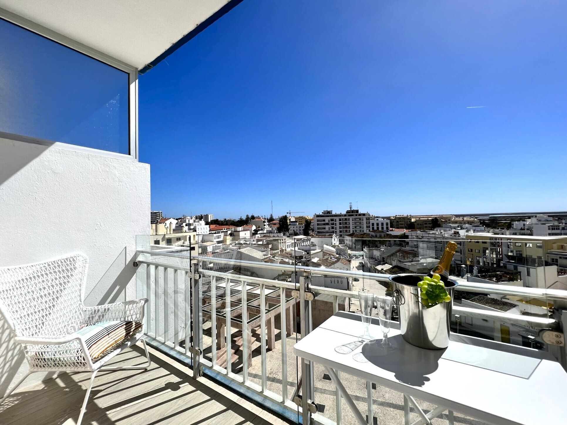 Un balcon avec une chaise blanche, une petite table et une bouteille de champagne.