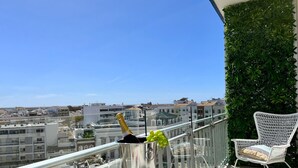 A balcony with a view of the city, a table with a champagne bottle, two glasses, and a vase with grapes. - Faro Deluxe by Homing (Faro)