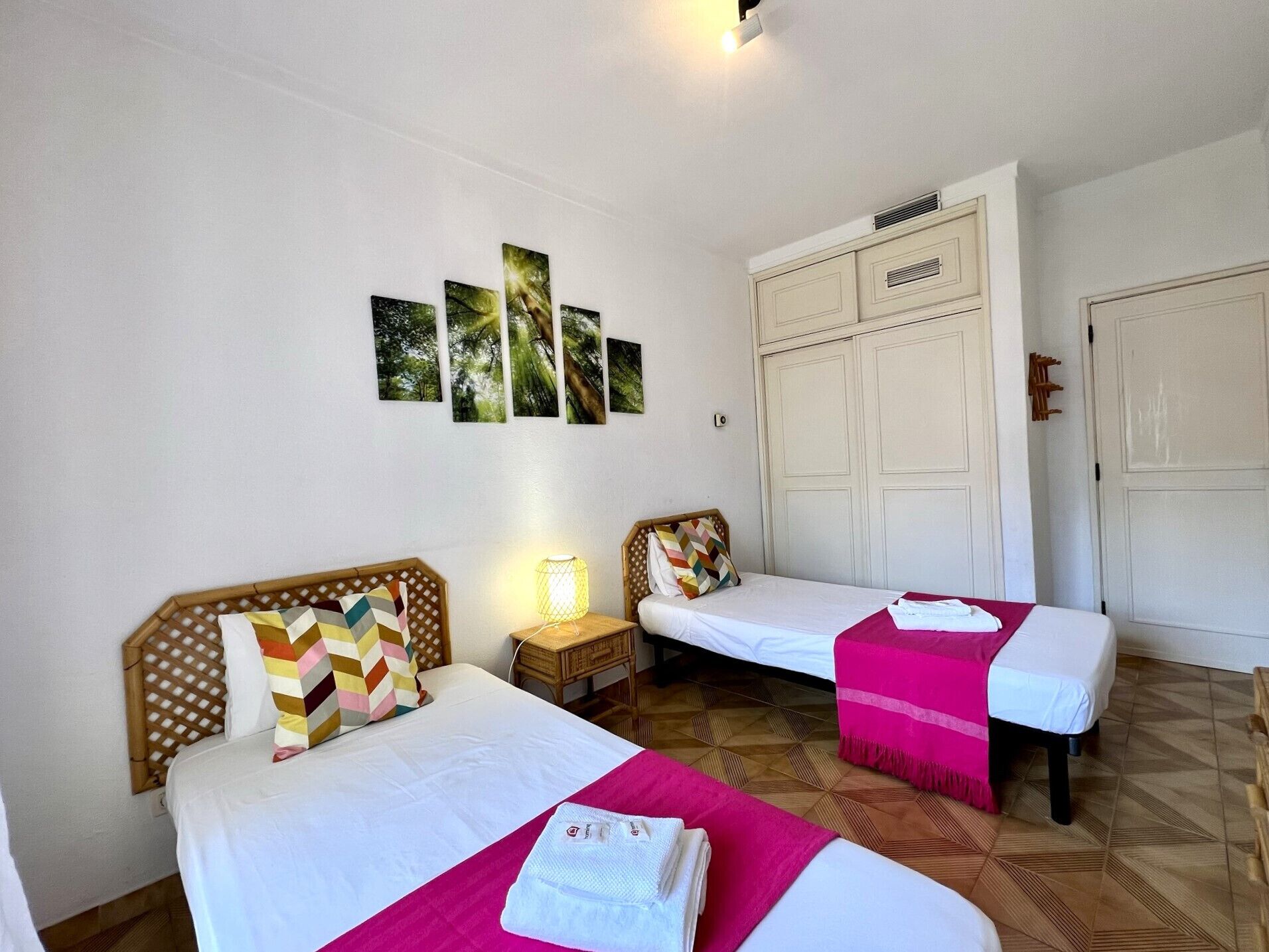 A hotel room with two beds, a wardrobe, and a wall with four framed pictures.