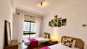 A hotel room with two beds, a large window with curtains, a wooden headboard, and artwork on the wall. - Vilamoura Palm Tree With Pool by Homing (Loulé)