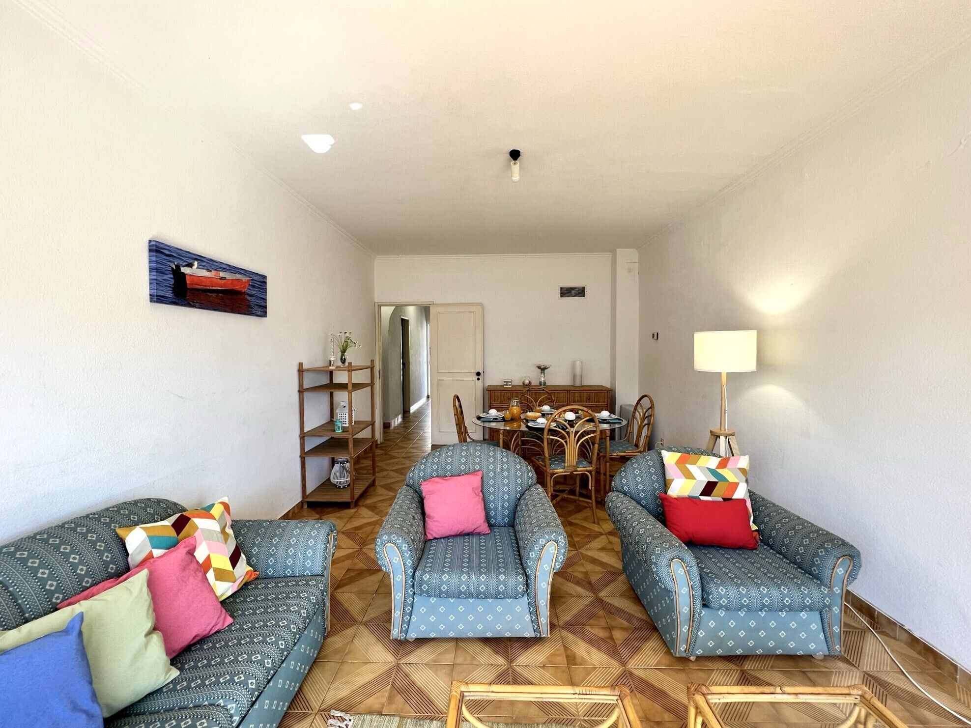 A living room with patterned sofas, a dining table, and a kitchen area in the background.