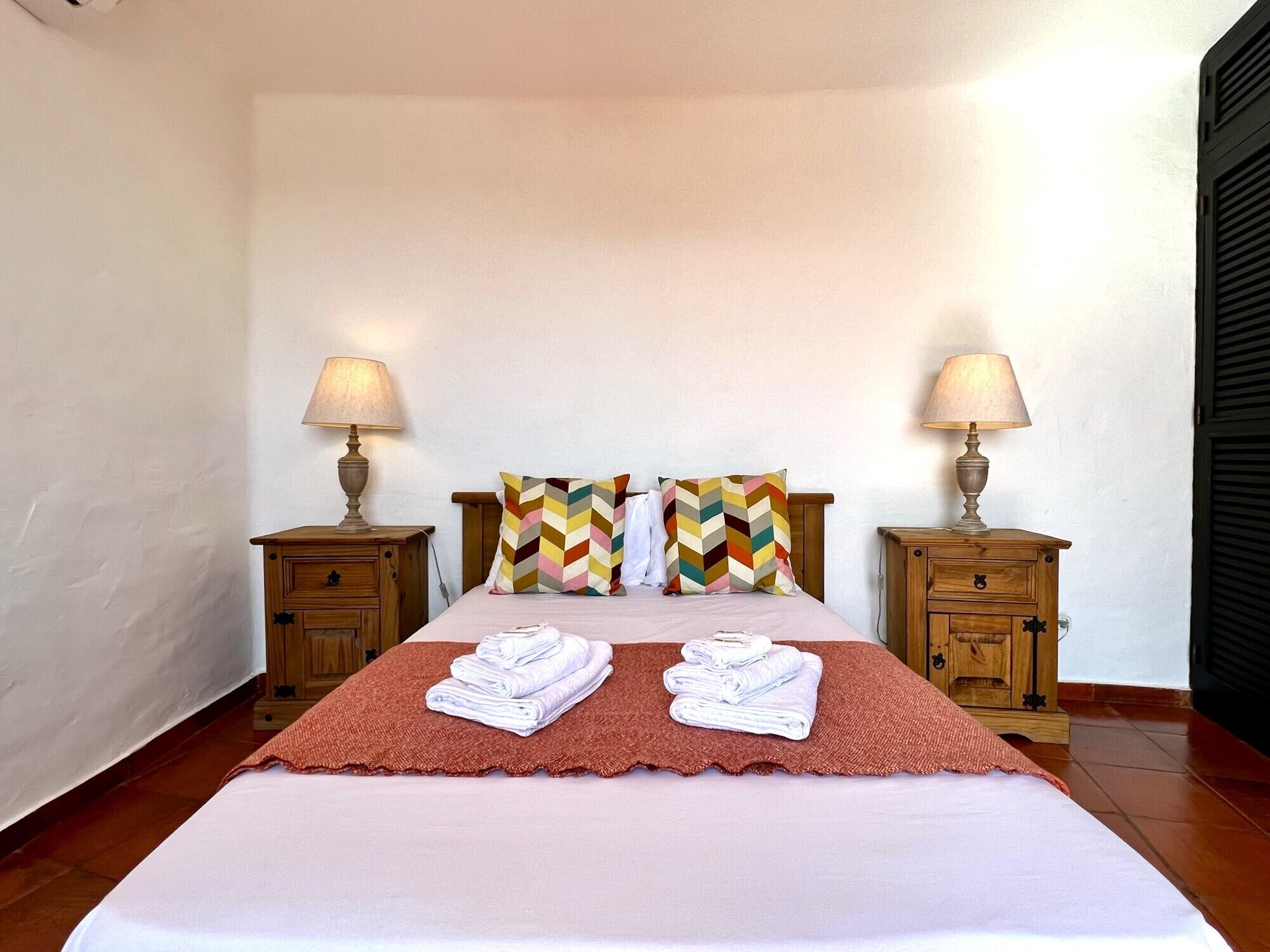 A neatly made bed with two pillows, two bedside tables with lamps, and a folded towel on the bed.