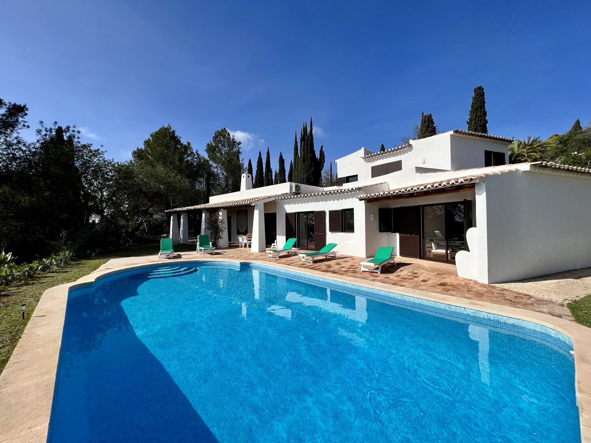 Une maison moderne dotée d’une piscine, de fauteuils de jardin verts et d’un espace patio.