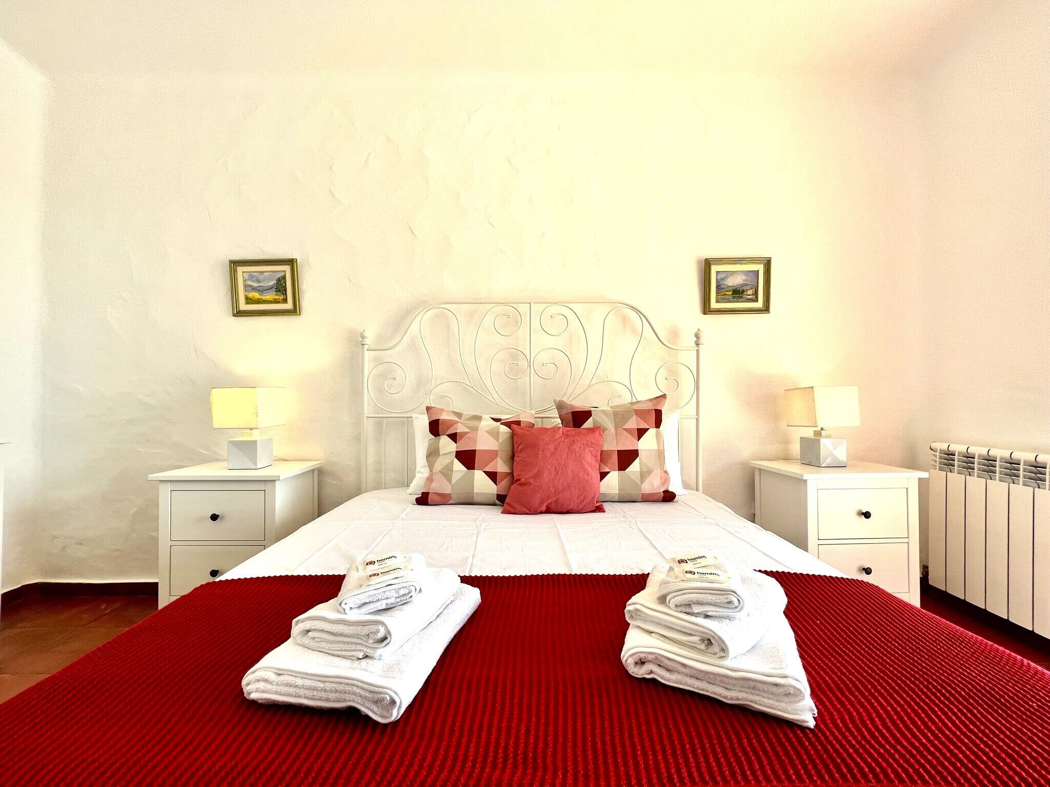 A neatly made bed with a red bedspread, two white bedside tables with lamps, and a headboard with the word "BAGGET" on it.