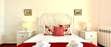 A neatly made bed with a red bedspread, two white bedside tables with lamps, and a headboard with the word "BAGGET" on it.