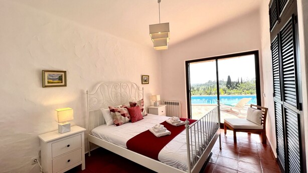 A bedroom with a bed, bedside table, lamp, and a view of an outdoor swimming pool. - Portimão Bellevue Villa With Pool (Portimão)