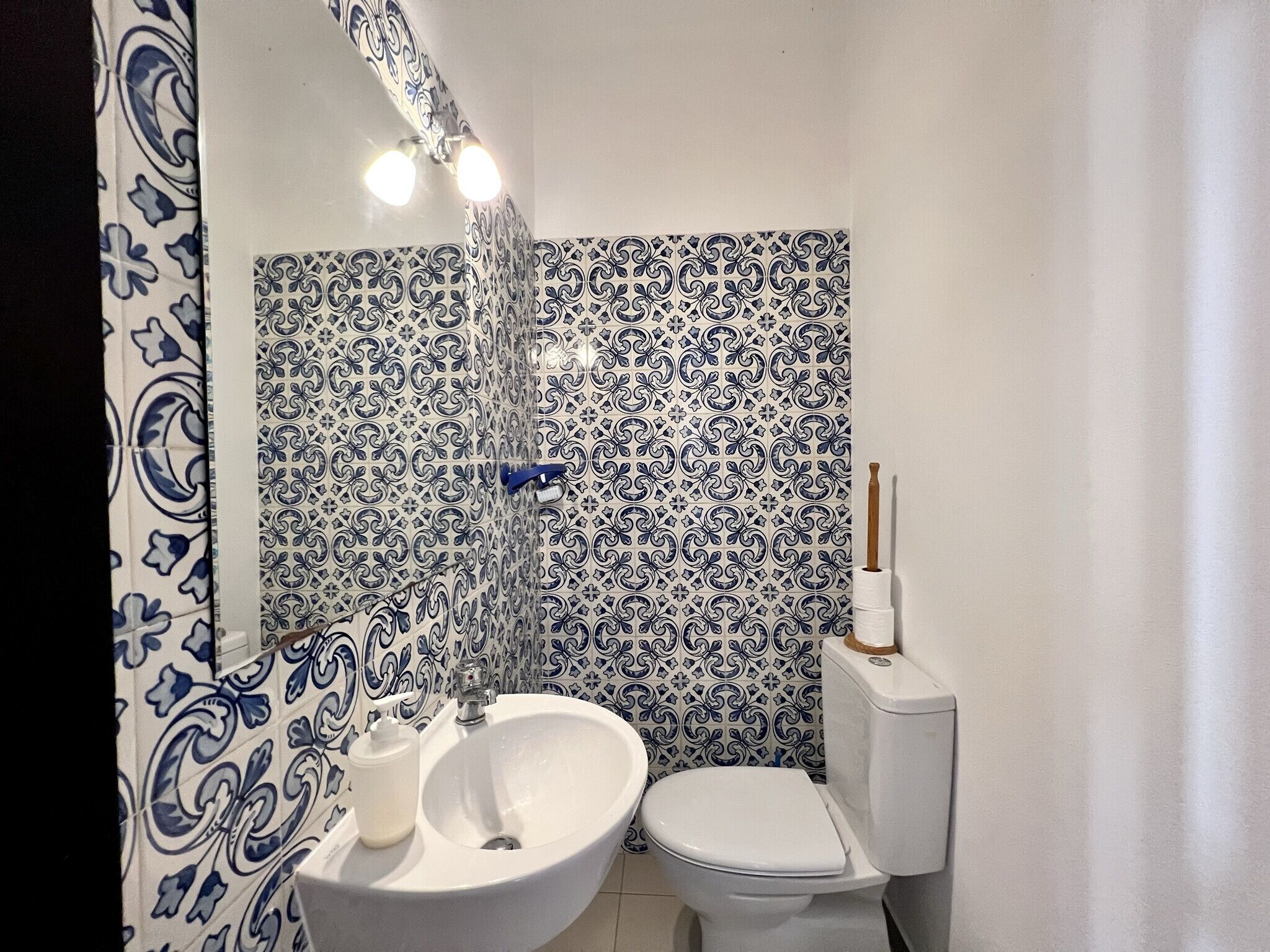 Ein Badezimmer mit einem weißen Waschbecken, einer Toilette und einer Dusche mit einer Wand aus blau-weißen Fliesen.