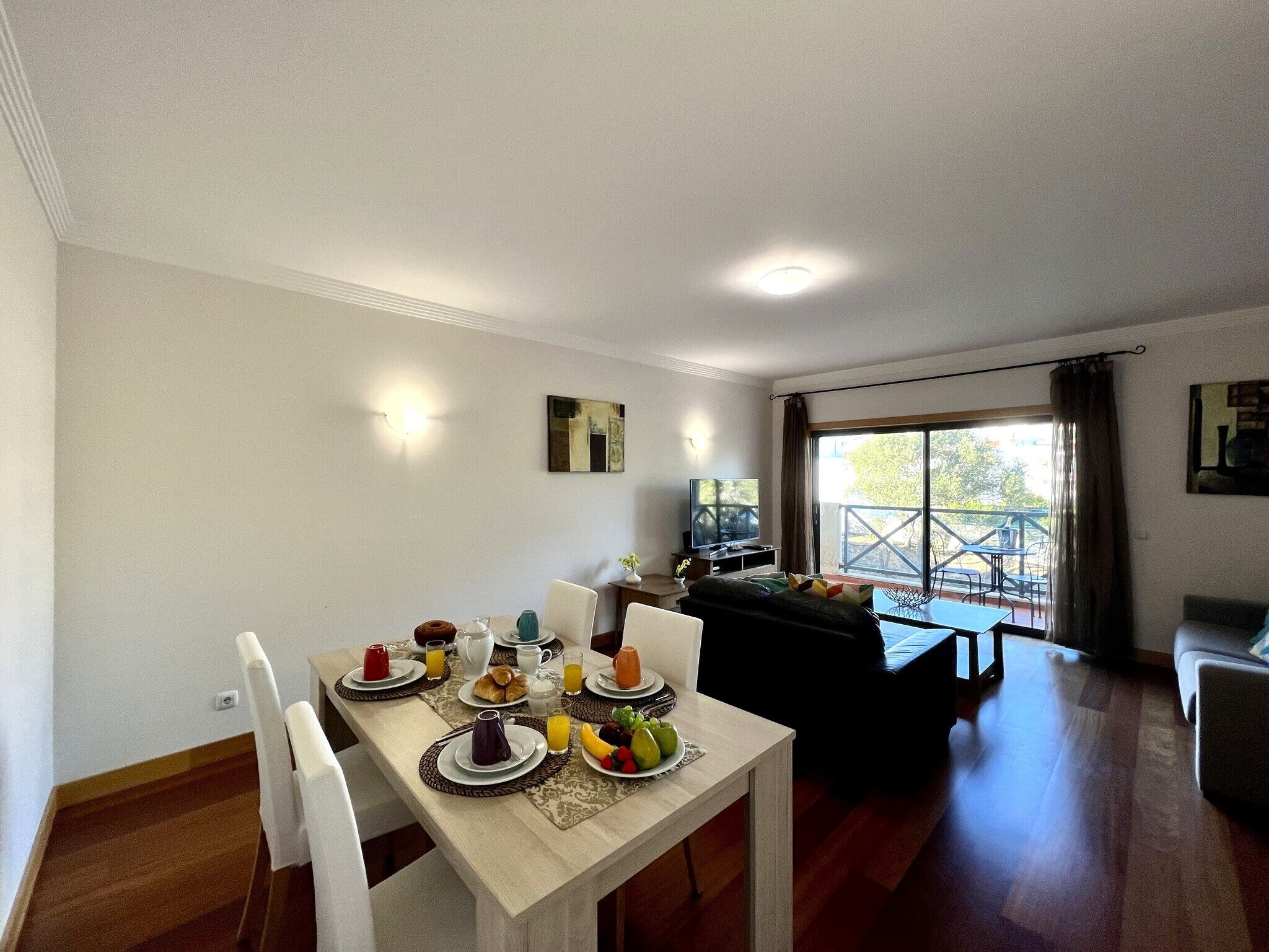 Ein Essbereich mit einem für das Frühstück gedeckten Tisch, einer Couch und einem Balkon mit Sitzgelegenheit.