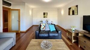 Un salon moderne avec un canapé en cuir noir, une table basse en bois et un téléviseur posé sur un meuble en bois.