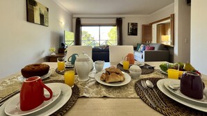 Une table dressée pour le petit-déjeuner, avec des assiettes, des tasses et une carafe de jus d’orange.