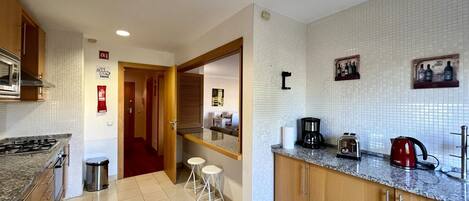 A modern kitchen with a microwave, stove, and coffee maker. There are stools and a small table in the center.