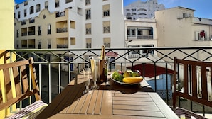 A balcony with a table set with a bottle of champagne, glasses, and a fruit bowl.