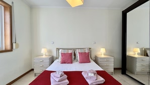 A bedroom with a bed, two bedside tables, a red rug, and a mirror.