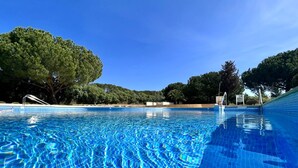 Una piscina azul cristalina con bordes de azulejos, rodeada de árboles y un cielo despejado.