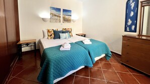 Un dormitorio con cama, dos mesitas de noche, cómoda y cuadros en la pared.