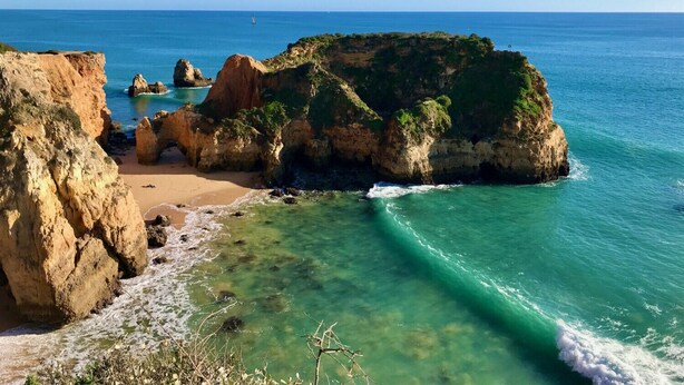 Un paisaje costero con acantilados rocosos, aguas turquesas cristalinas y una playa arenosa.