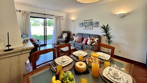 Un comedor con una mesa dispuesta para el desayuno, un sofá al fondo y vistas al exterior.