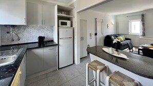 A modern kitchen with white cabinets, a microwave, a refrigerator, and a granite countertop.