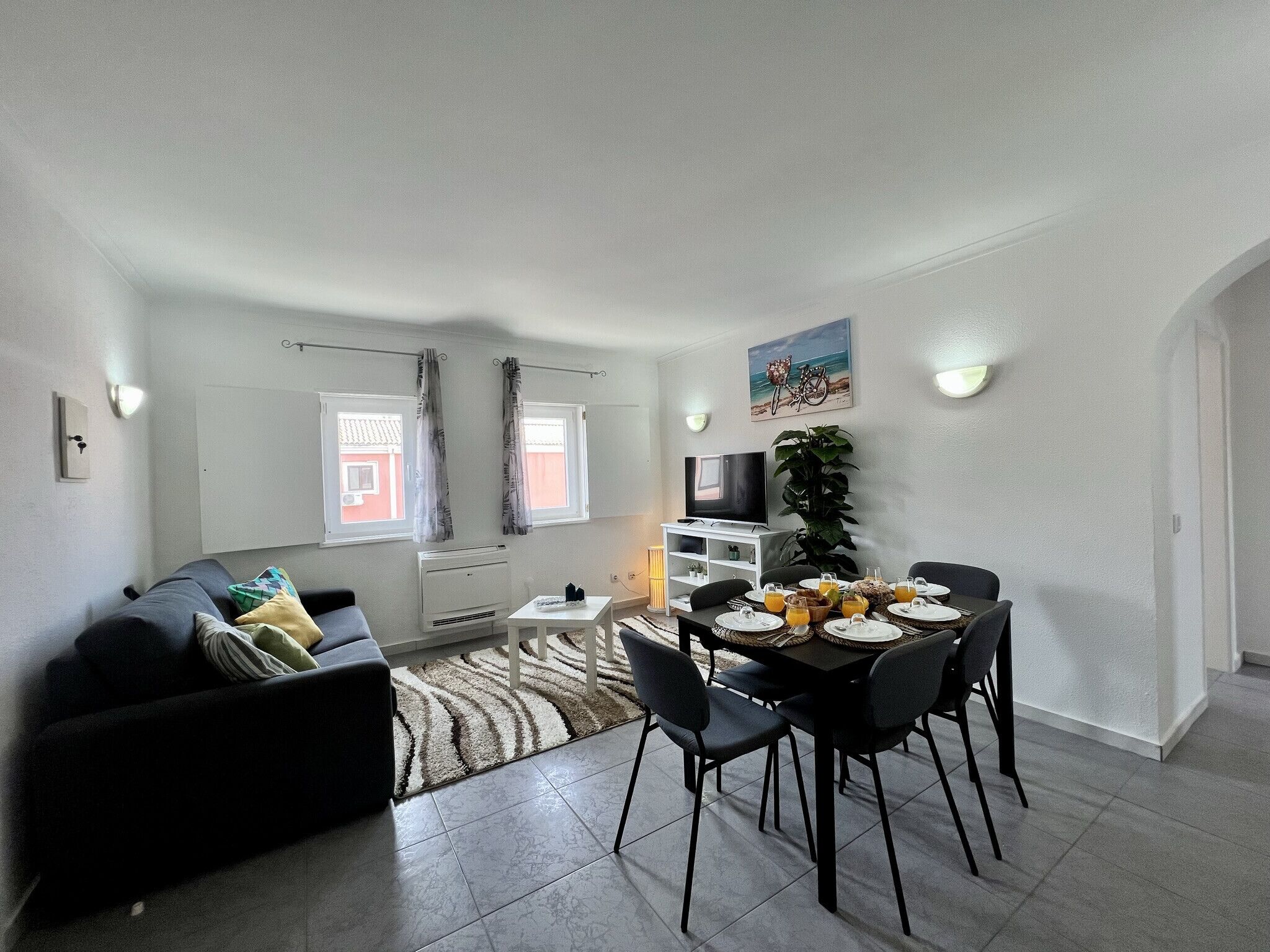 A compact living space with a dining area, a sofa, a TV, and a view of the outside.