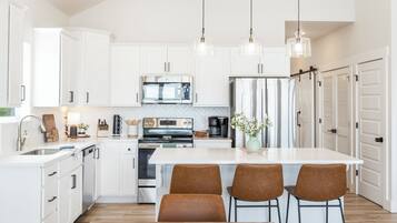 A modern kitchen with white cabinetry, stainless steel appliances, a central island with bar stools, and pendant lighting.