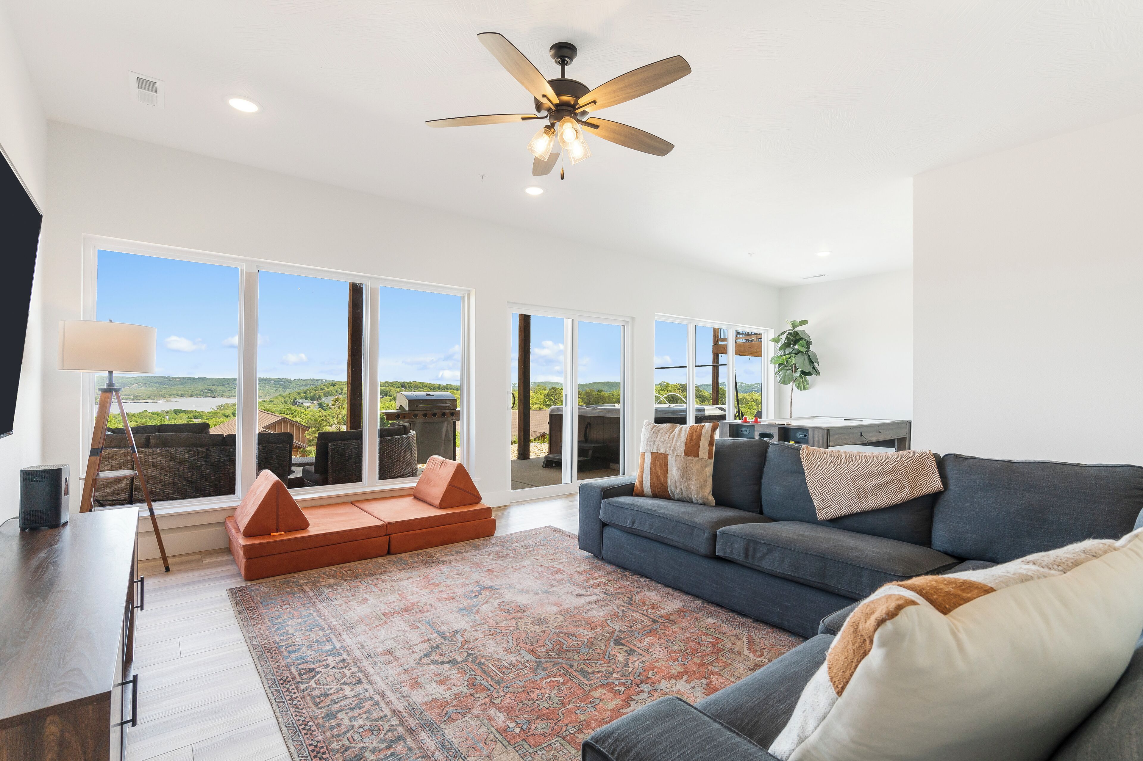 A spacious living room with a large gray sofa, a patterned rug, and a ceiling fan.