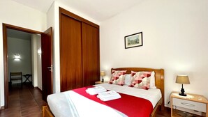 A neatly arranged hotel room with a bed, bedside table, and a door leading to another room. - Vilamoura SEA Village by Homing (Loulé)