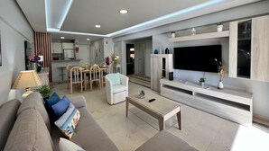 A modern living room with a sofa, coffee table, TV, and kitchen in the background. - Vilamoura Marina MAR 2 With Pool (Loulé)