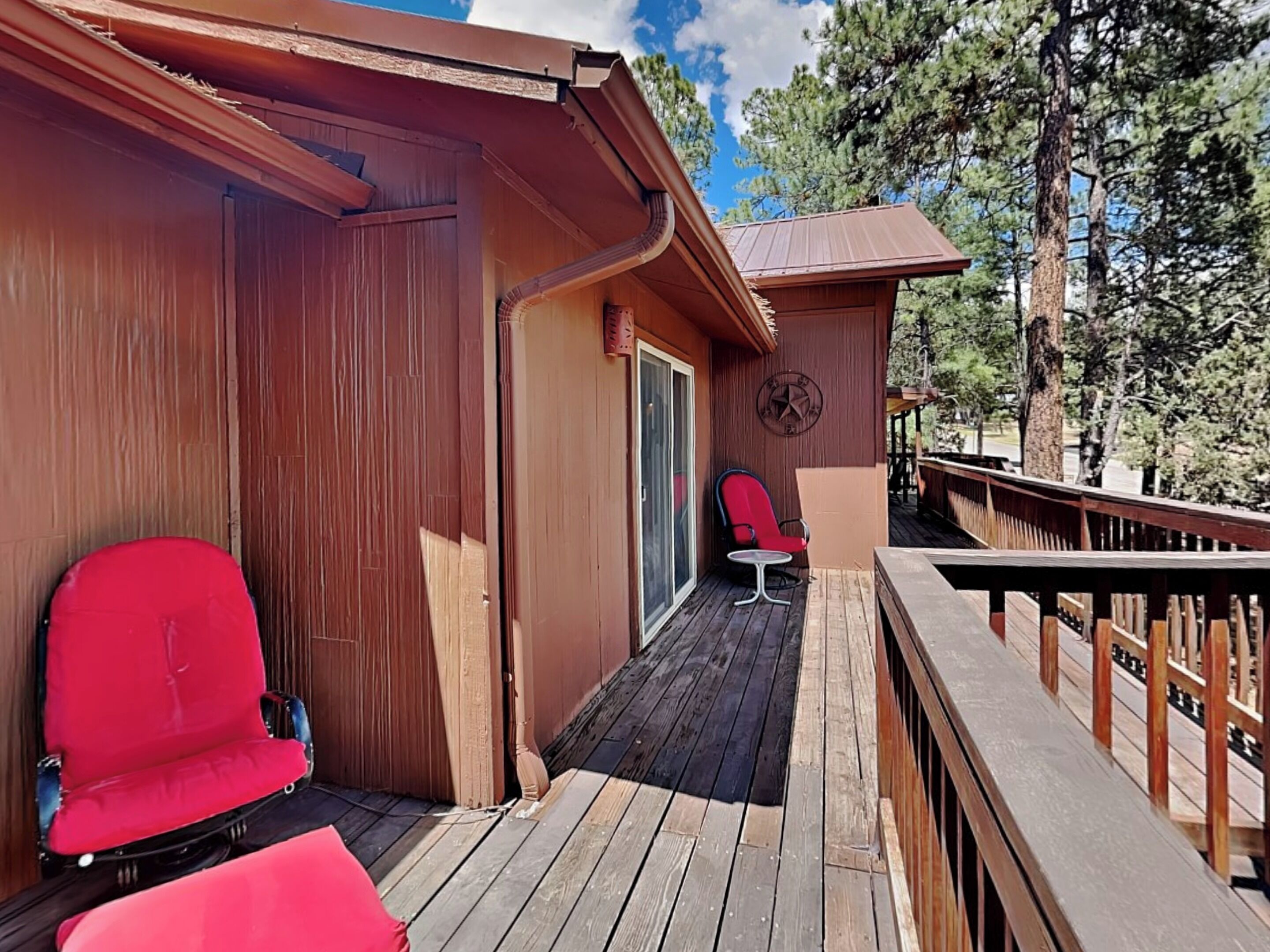 A wooden deck with two red chairs and a small table.