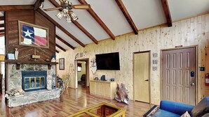 Un salon spacieux avec une cheminée en pierre, des murs en bois, un téléviseur et un canapé bleu.
