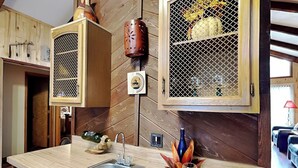 Une cuisine avec des meubles de rangement en bois, un évier et un plan de travail sur lequel se trouvent un verre à vin et des raisins.