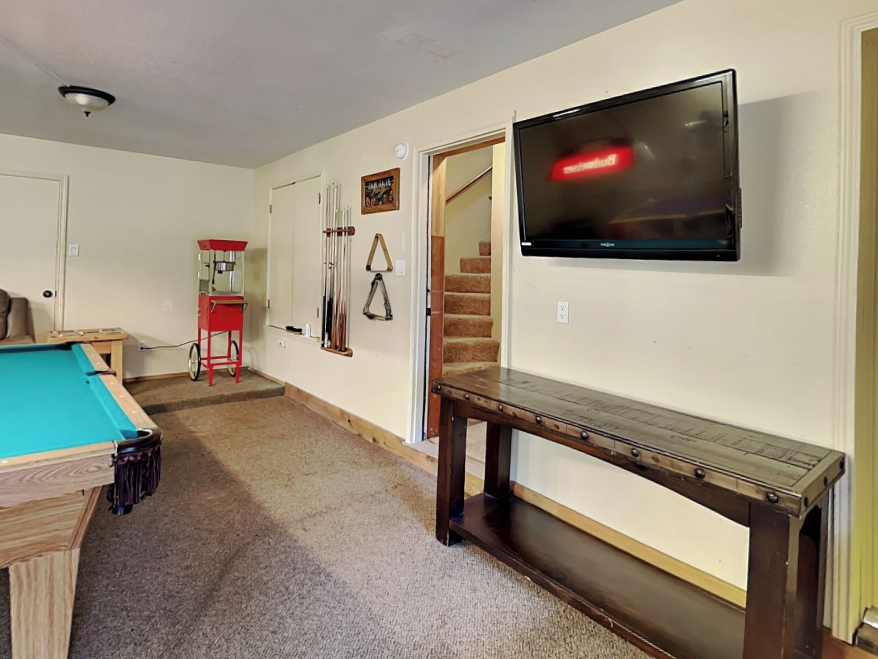 A room with a pool table, a billiards rack, a TV mounted on the wall, and a staircase leading to another level.