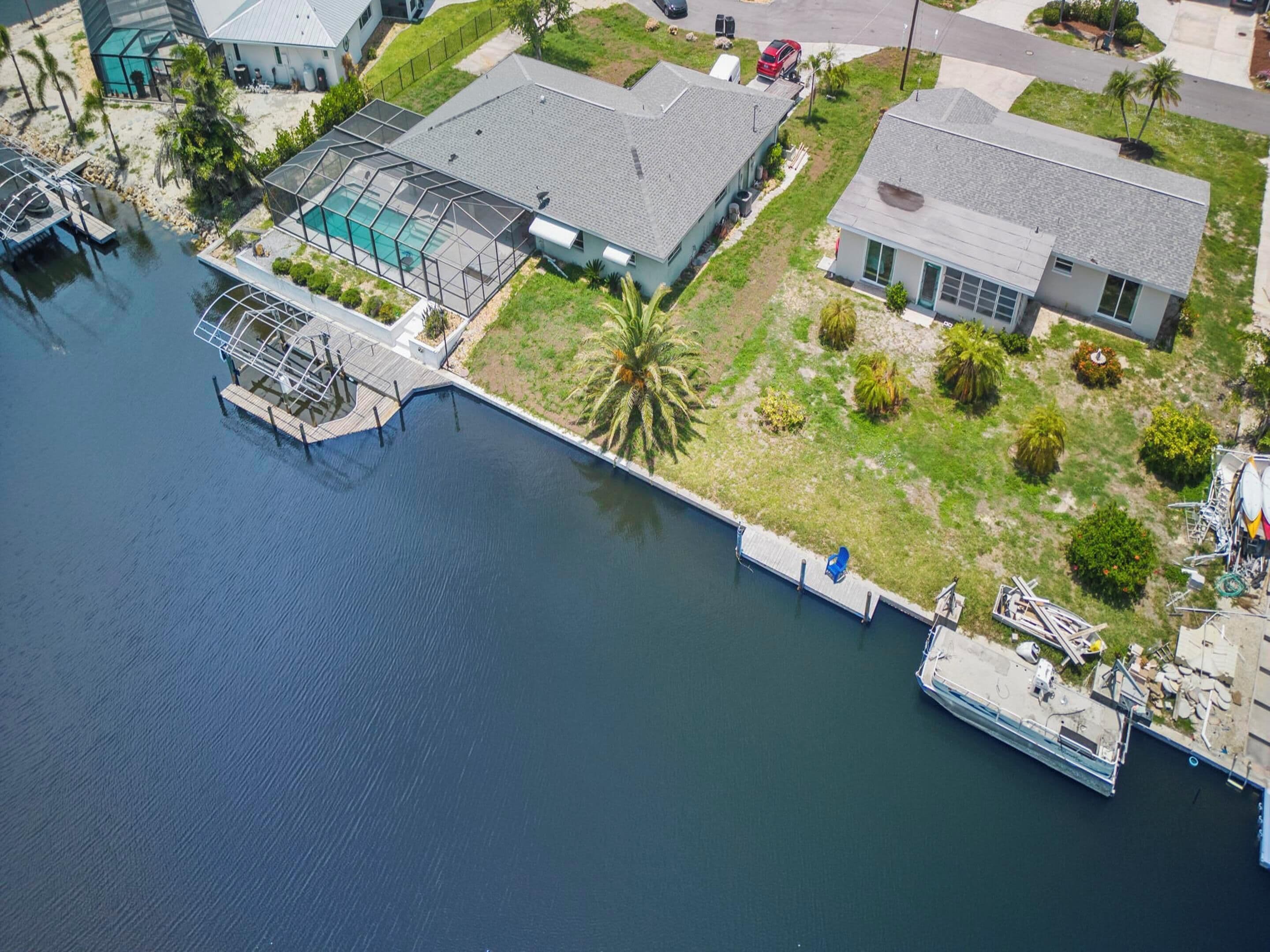 An aerial view of a waterfront property with a swimming pool, dock, and adjacent houses.