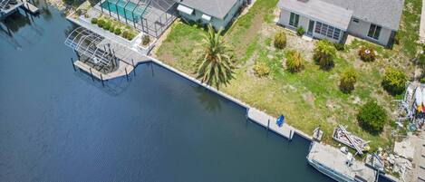 An aerial view of a waterfront property with a swimming pool, dock, and adjacent houses.