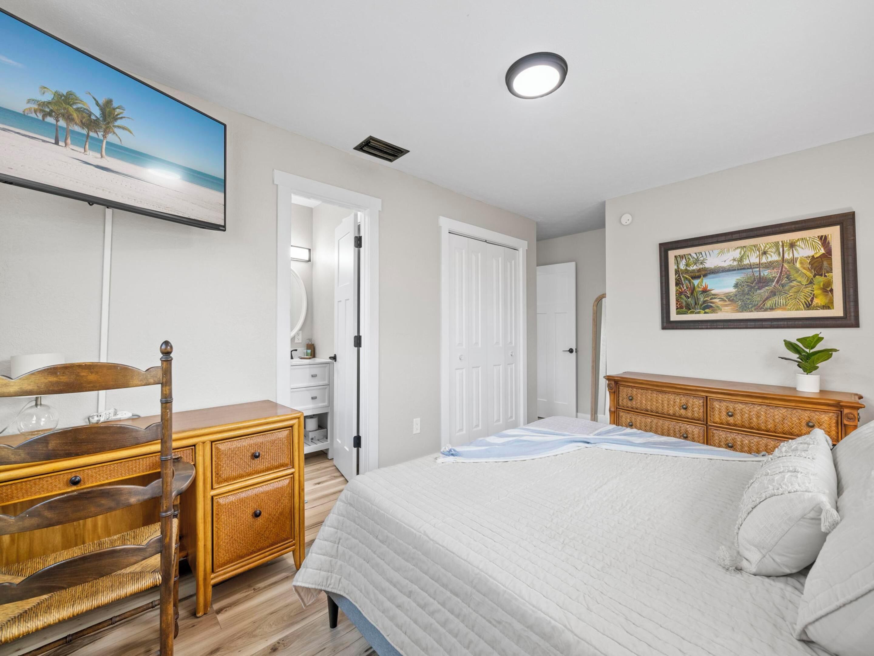 A bedroom with a bed, a dresser, a mirror, a door, and a painting of a beach scene.