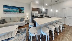 A modern kitchen with a central island, bar stools, and a dining table. - Breezy Villa by Distinctive Beach Rentals (Palm Coast)