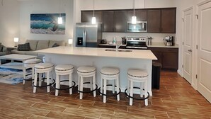 A modern kitchen with a central island, bar stools, stainless steel appliances, and pendant lighting. - Breezy Villa by Distinctive Beach Rentals (Palm Coast)