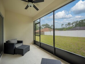 A covered patio area with a ceiling fan, a seating area with cushions, and a view of a grassy yard. - Breezy Villa by Distinctive Beach Rentals (Palm Coast)