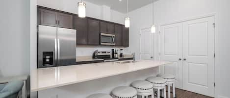 A modern kitchen with stainless steel appliances, a white countertop, and bar stools.