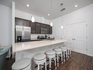 A modern kitchen with stainless steel appliances, a white countertop, and bar stools.