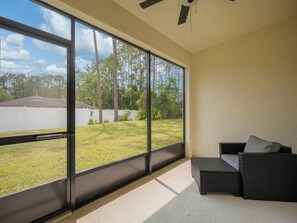 A room with large windows, a ceiling fan, and a wicker sofa with cushions. - Breezy Villa by Distinctive Beach Rentals (Palm Coast)