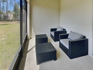 A covered outdoor seating area with wicker furniture and a view of a grassy yard. - Breezy Villa by Distinctive Beach Rentals (Palm Coast)