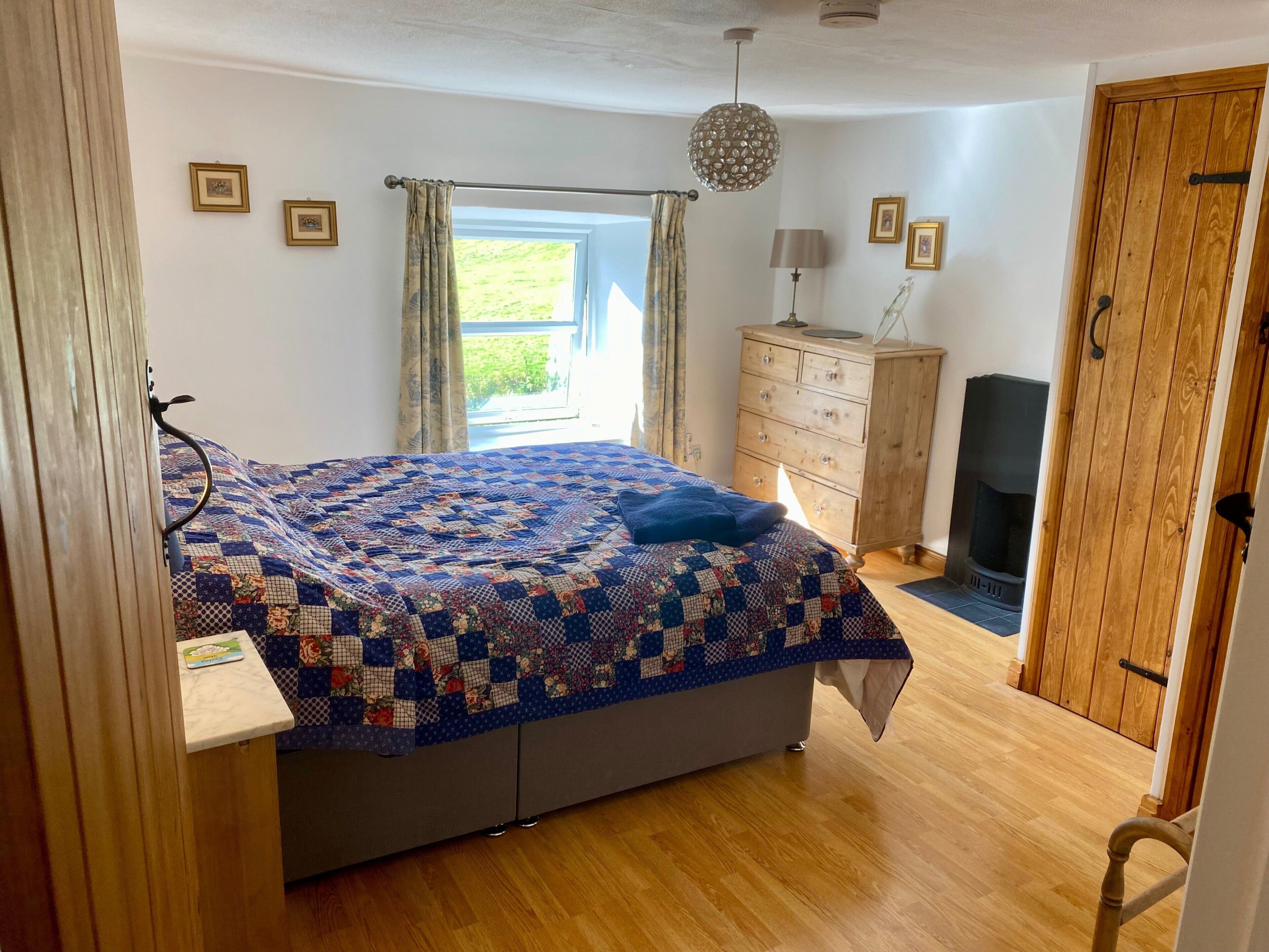Een slaapkamer met een bed, een dressoir, een lamp en uitzicht op de omgeving.