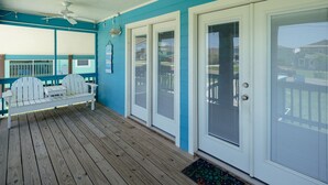 A covered porch with wooden flooring, white doors with screens, and a ceiling fan. - Turtle's Nest by Miss Kitty’s (Rockport)