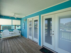 A covered porch with wooden flooring, white doors with screens, and a ceiling fan. - Turtle's Nest by Miss Kitty’s (Rockport)