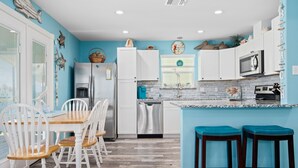 A kitchen with white cabinets, a wooden dining table with white chairs, and a blue accent wall. - Turtle's Nest by Miss Kitty’s (Rockport)
