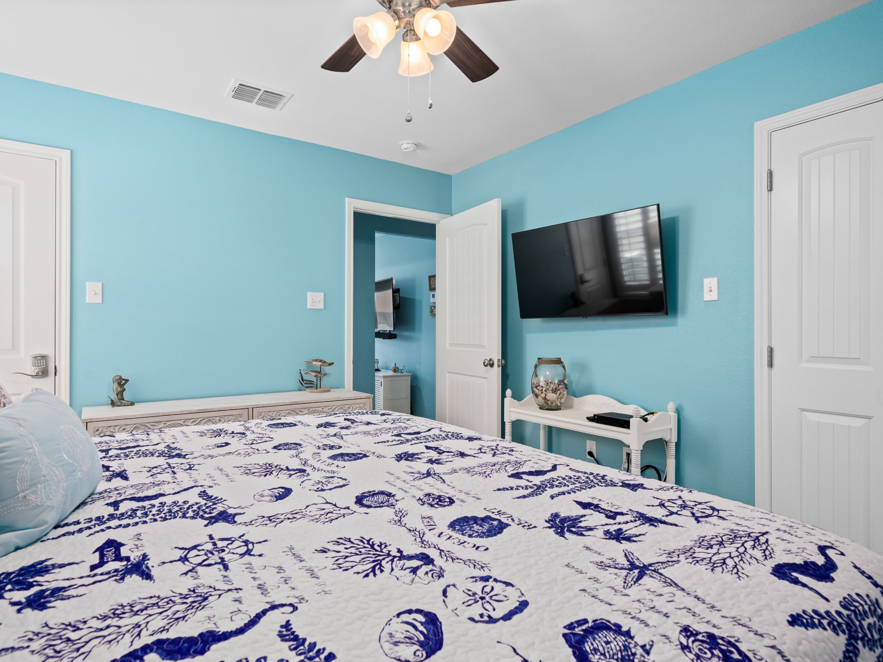 A bedroom with a bed, a ceiling fan, a TV, and a dresser.
