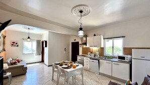 A modern kitchen with white cabinets, a dining table with chairs, and a refrigerator. - Tavira Vila Formosa 5 With Pool (Tavira)