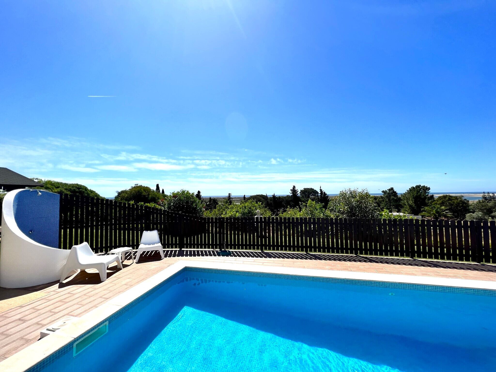 A rectangular swimming pool with a wooden deck and white lounge chairs.