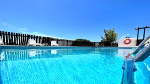 A clear blue swimming pool with a tiled deck, white lounge chairs, and a wooden fence in the background. - Tavira Vila Formosa 3 With Pool (Tavira)