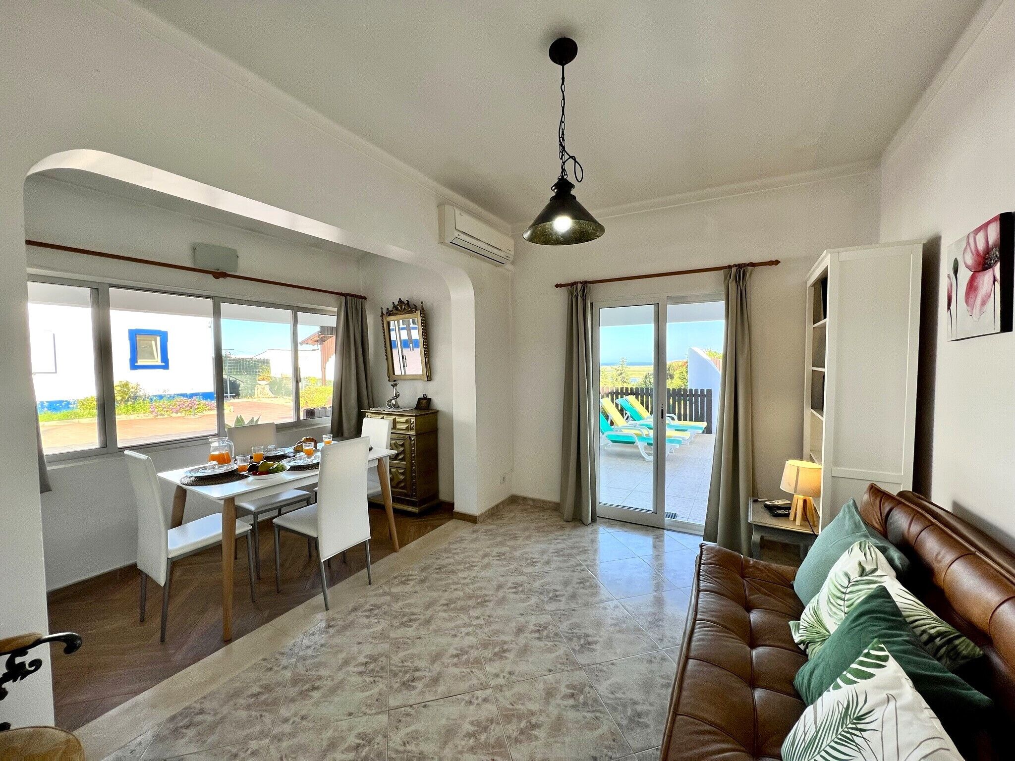 A spacious living area with a dining table, a sofa, and a view of the outdoor pool.